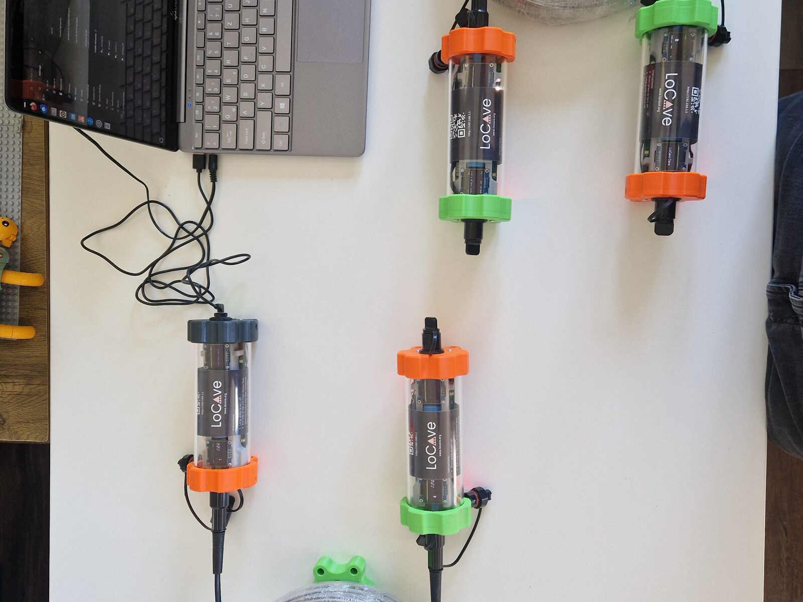 A laptop on a bench connected by a USB cable to a LoCave node, with three more nodes and two coils of fibre laid out beside it.